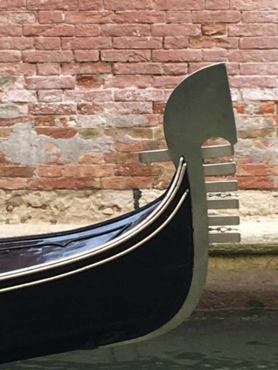 A gondola parked by a brick wall highlights its sleek design, oar, and ornate features typical of Venetian craftsmanship.
